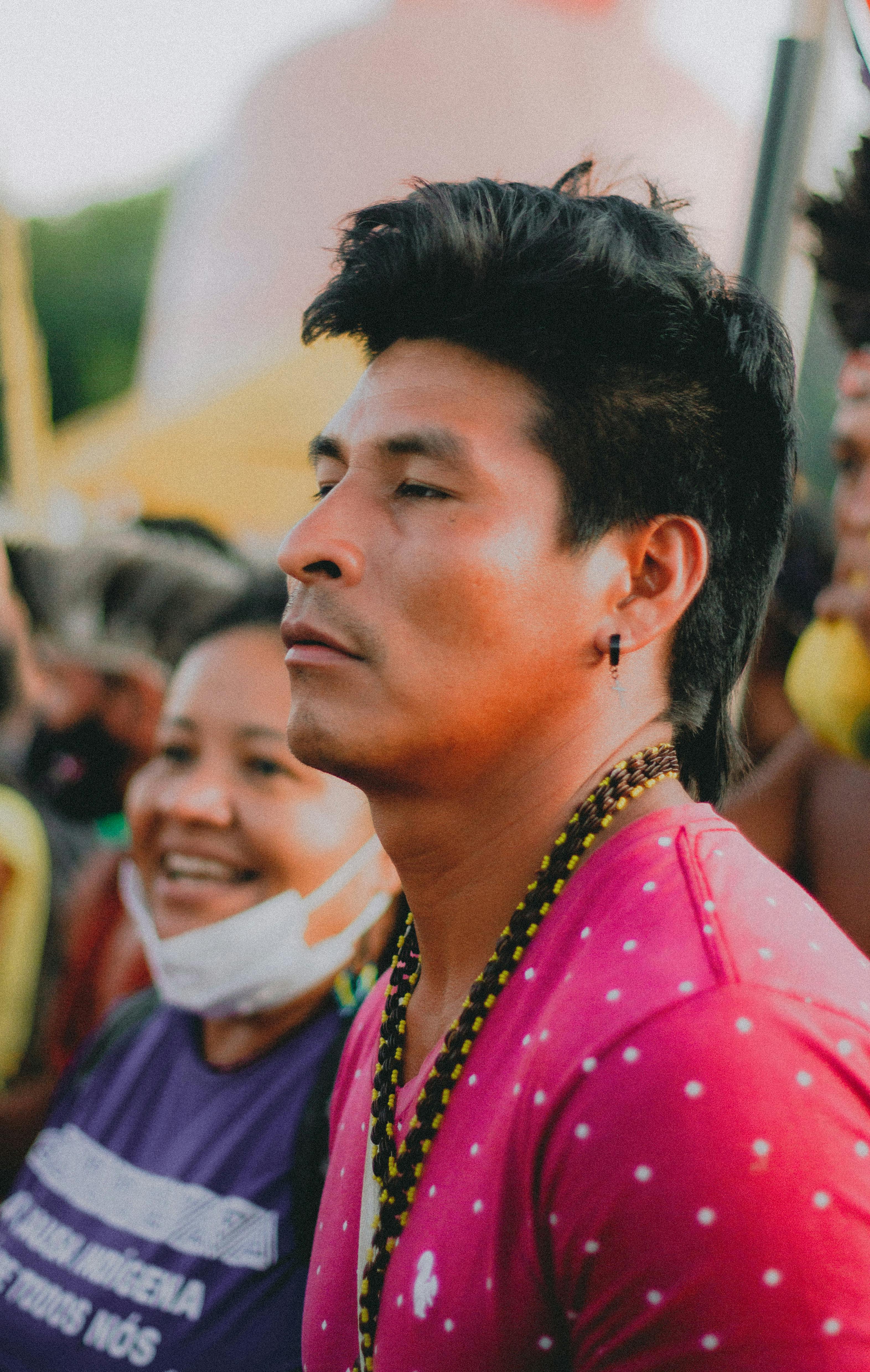 Close-up portrait of a man at a festival, wearing a pink polka dot shirt and bead necklace.