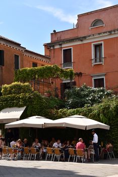 Outdoor café in Venice with people enjoying meals beside vibrant buildings.