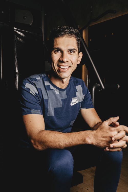 Free Smiling man seated indoors, wearing blue athletic shirt, photographed in a relaxed pose. Stock Photo