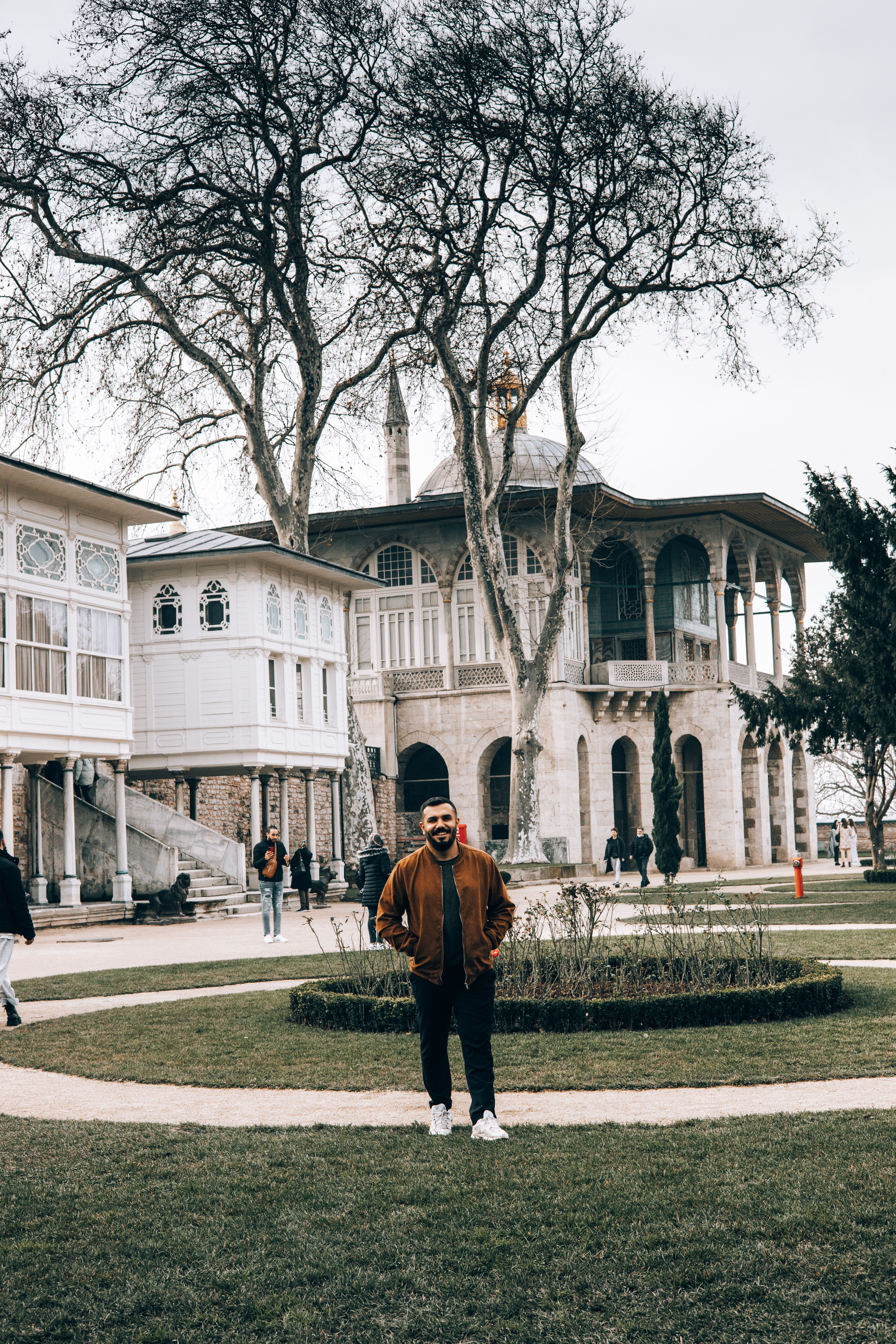 A man standing in front of the historic Topkapi Palace in Istanbul with trees and architectural details visible.