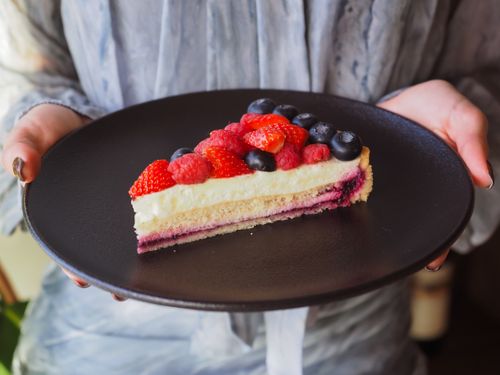 Free A close-up of a berry-topped cheesecake slice on a black plate, perfect for dessert lovers. Stock Photo