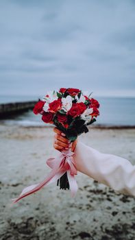 A hand holding a vibrant bouquet of roses against the scenic beach in Kaliningrad.