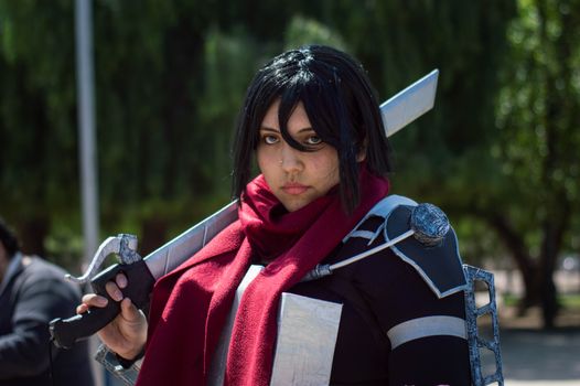 A focused cosplayer in detailed costume poses with a sword outdoors.