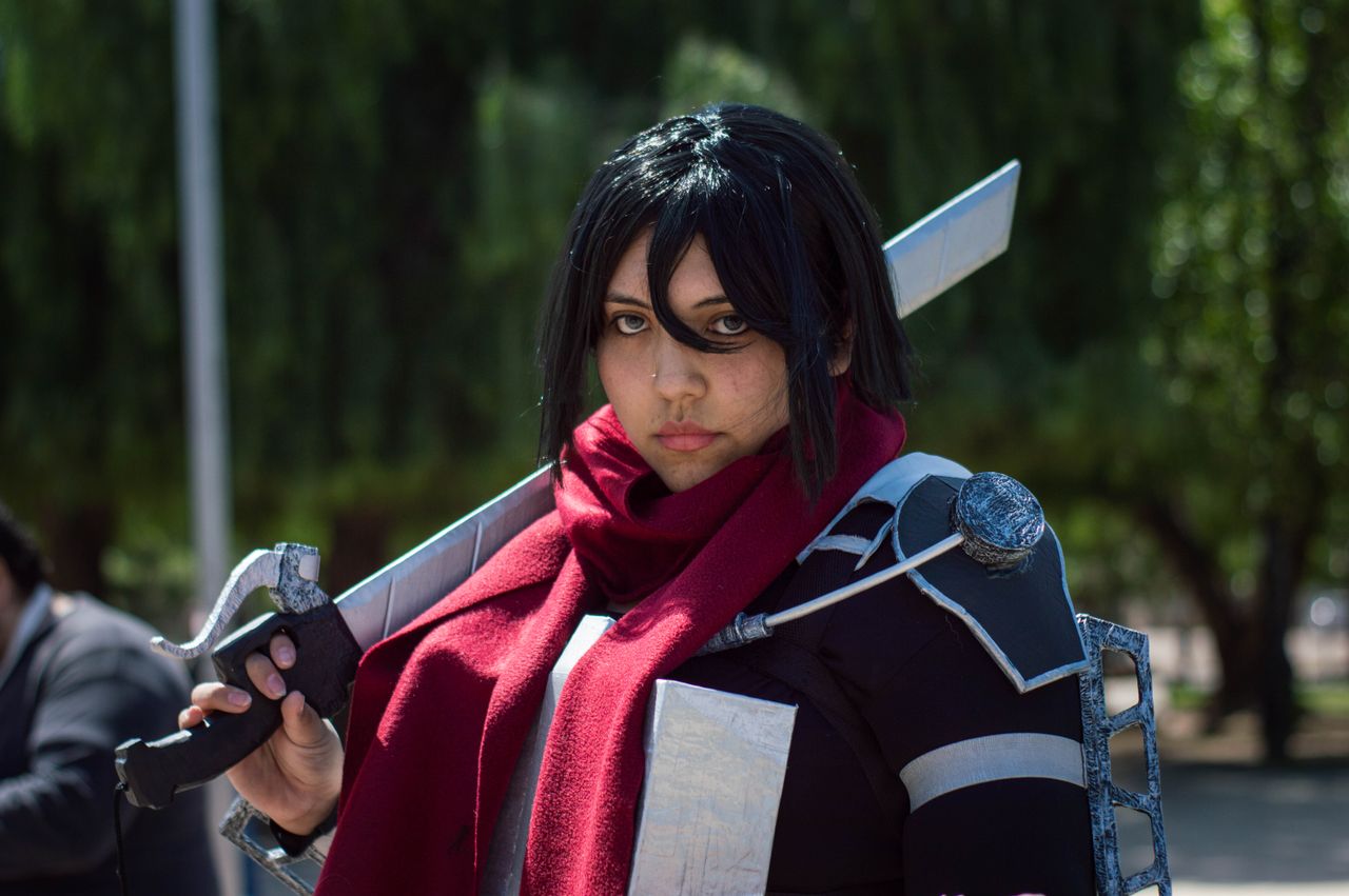 a focused cosplayer in detailed costume poses with a sword outdoors