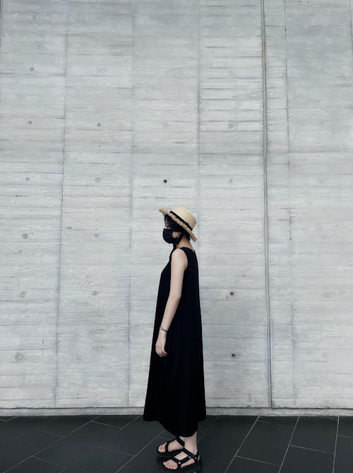 Woman in Black Sleeveless Dress Standing Beside a Wall