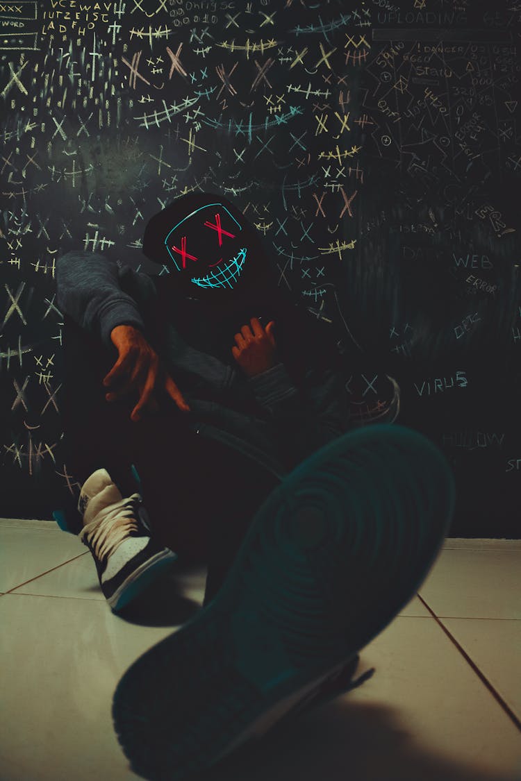 Person With Face Sewn On Mask Sitting Under Wall