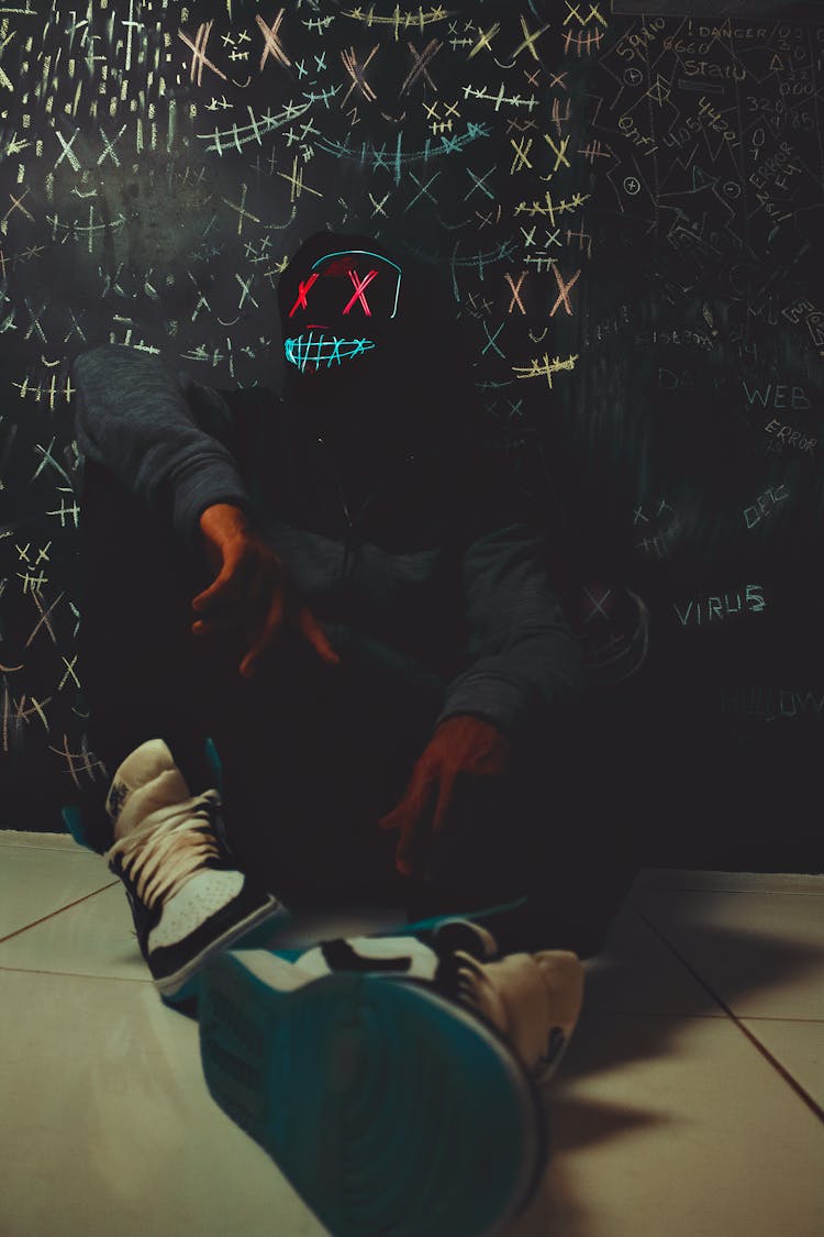 Person Wearing Black Mask Sitting And Leaning Against Grafitti Wall