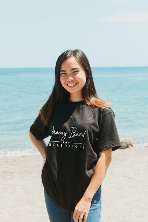 Teenage Girl Smiling in Black Shirt and Denim Jeans Standing on Seashore