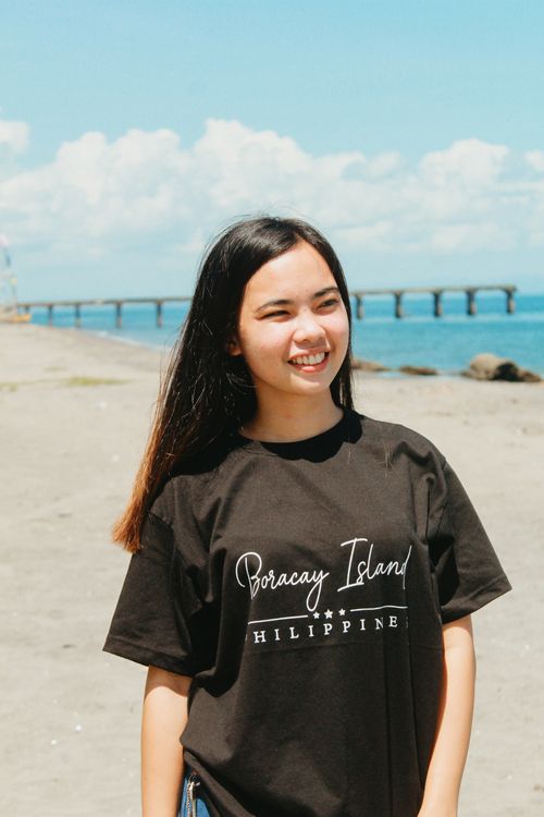 Free Young woman enjoying a sunny day at the beach, wearing a Boracay Island T-shirt. Stock Photo