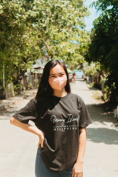 Free Woman wearing a mask and Boracay Island t-shirt posing outdoors under the bright sun. Stock Photo