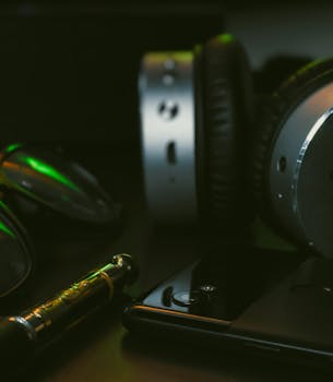 Close-up view of modern gadgets including headphones, smartphone, and eyeglasses on a desk.