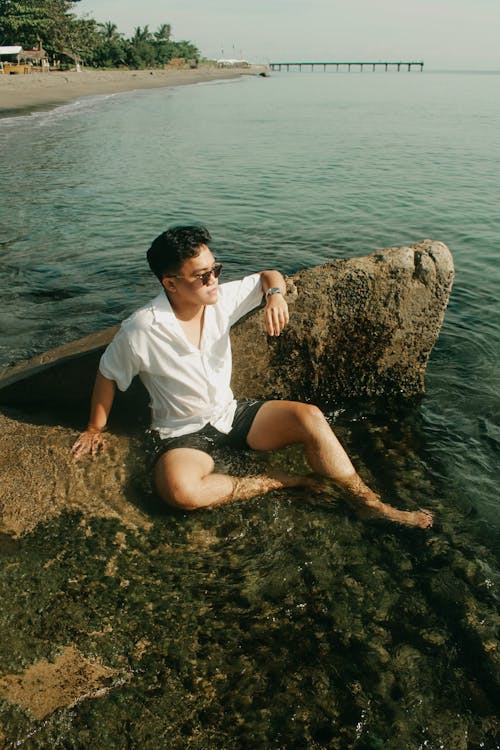 Man Sitting on Shallow Water Beside a Rock