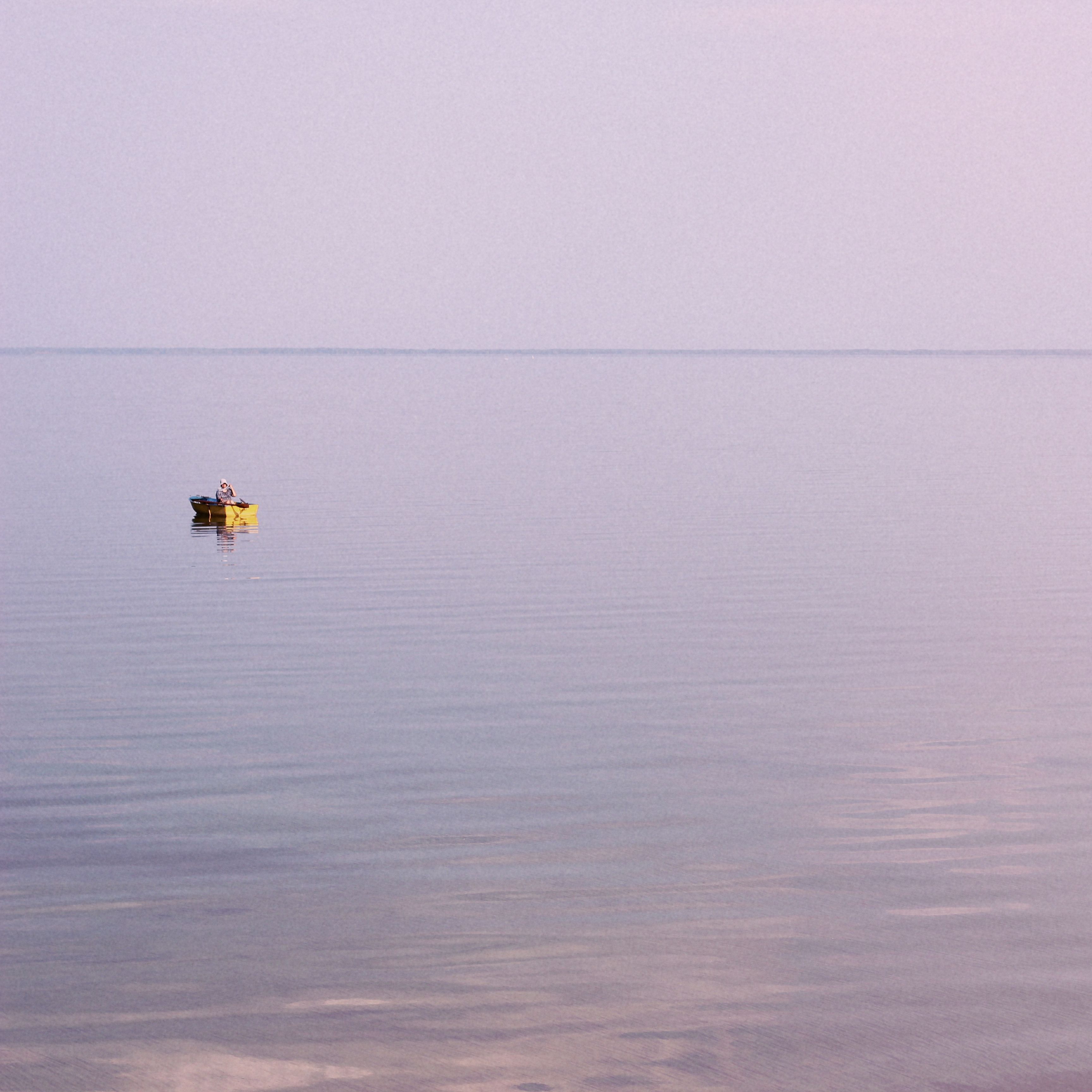 A lone yellow boat floats on a tranquil sea under a pastel sky, evoking serenity.