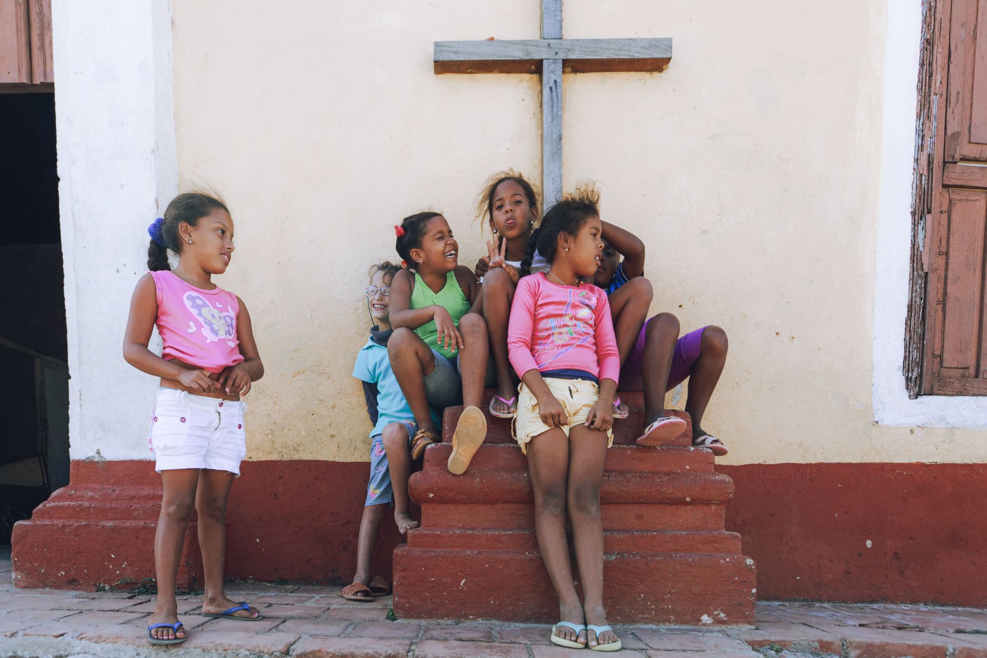 Group of diverse young girls sitting and chatting by an urban wall under a cross.