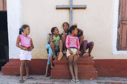 Free Group of diverse young girls sitting and chatting by an urban wall under a cross. Stock Photo