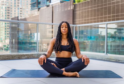 Free African American woman meditating on a terrace in Dubai, wearing activewear and sitting with eyes closed. Stock Photo