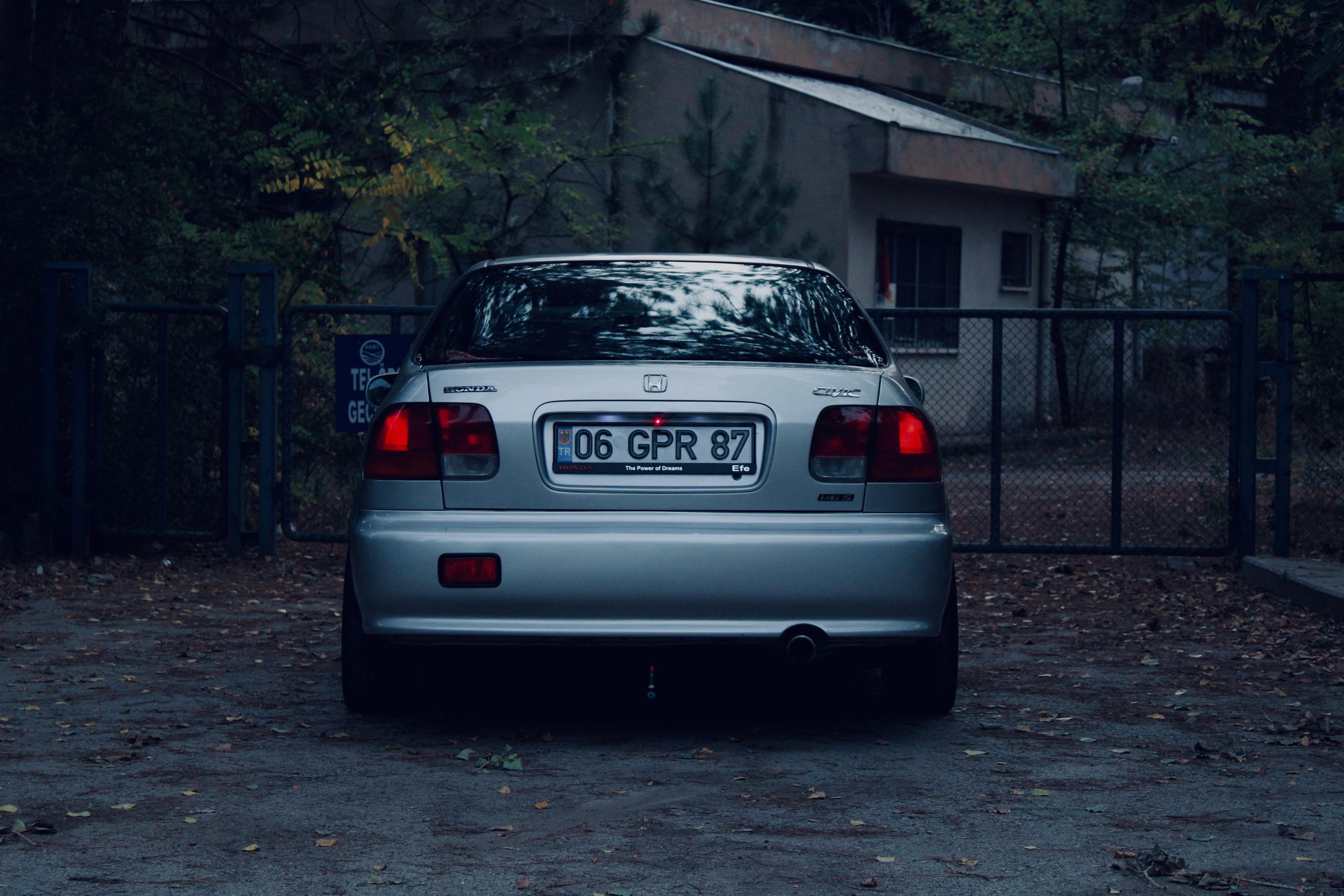 Silver Honda car parked outdoors in Turkey, surrounded by green trees and a metal gate.