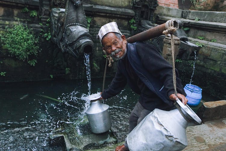 Old Man Near Water In Steel Containers