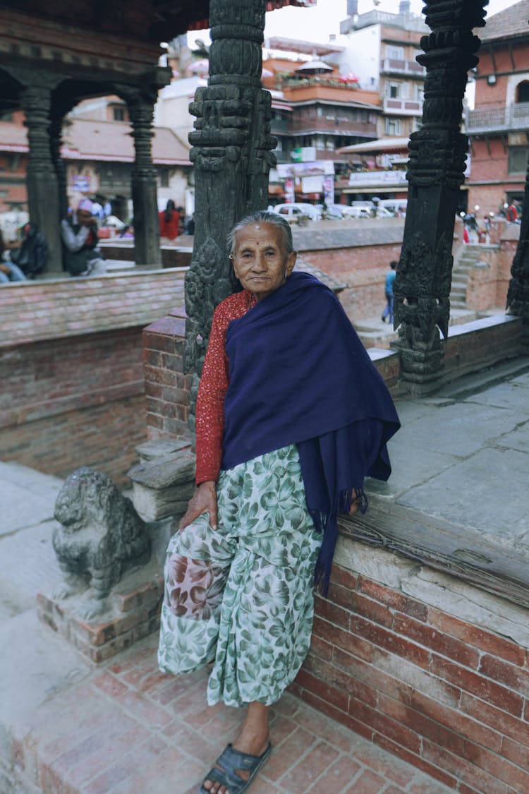 Elderly Woman Sitting Beside A Pillar