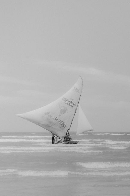 Black and white photo of a sailboat on ocean waves at Canoa Quebrada, Brazil.