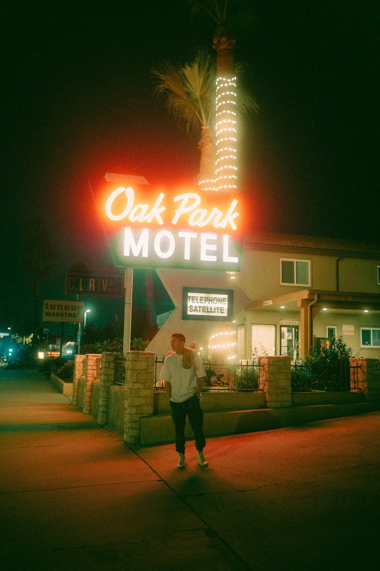 Man Standing In Front Of Motel Neon Sign