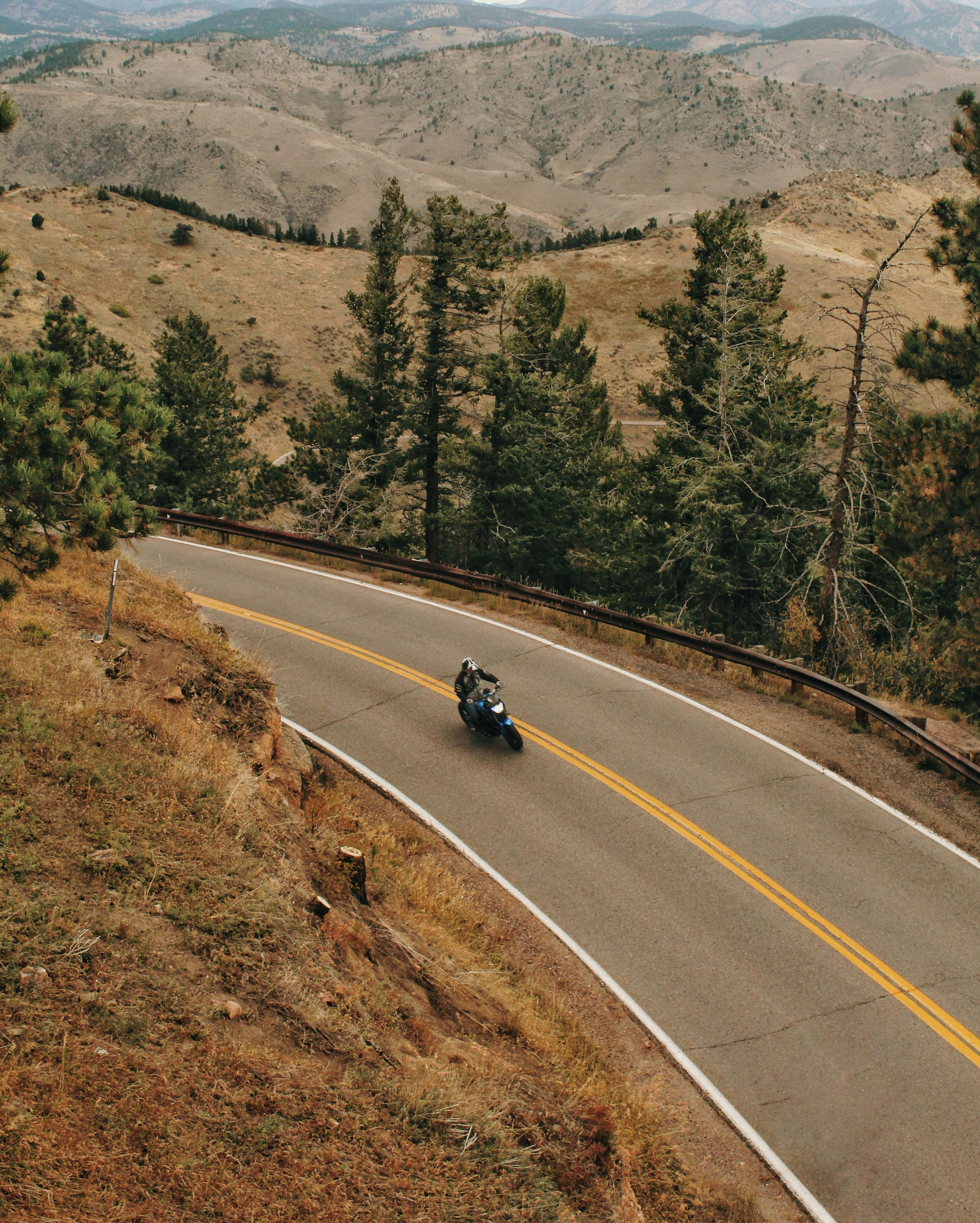 Biker rides along a winding mountain road with lush trees and hills in the backdrop.