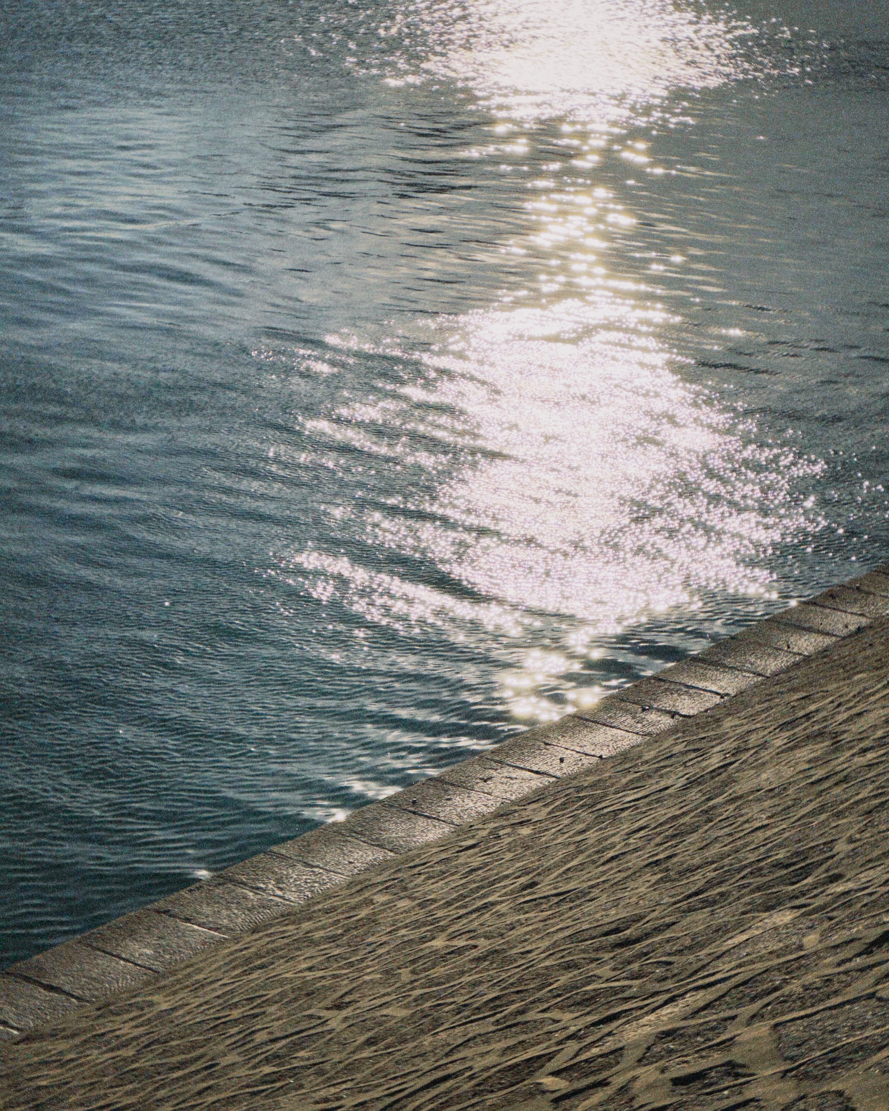 Peaceful water scene with sunlight reflecting on stone waterfront.