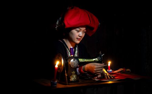 Free Asian woman sewing with a vintage machine in a dark room lit by candlelight. Stock Photo