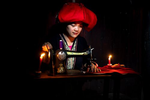 Free Asian woman sewing by candlelight, showcasing traditional skills and attire. Stock Photo
