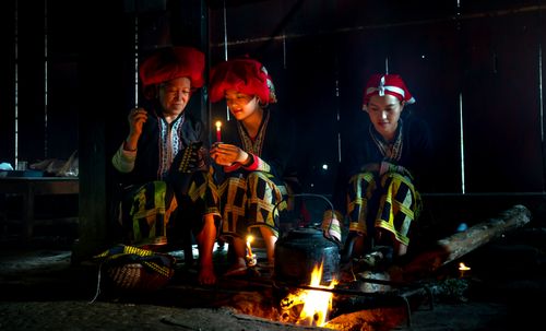 Free A serene scene of three Asian adults in traditional attire, sitting by a warm indoor fire. Stock Photo