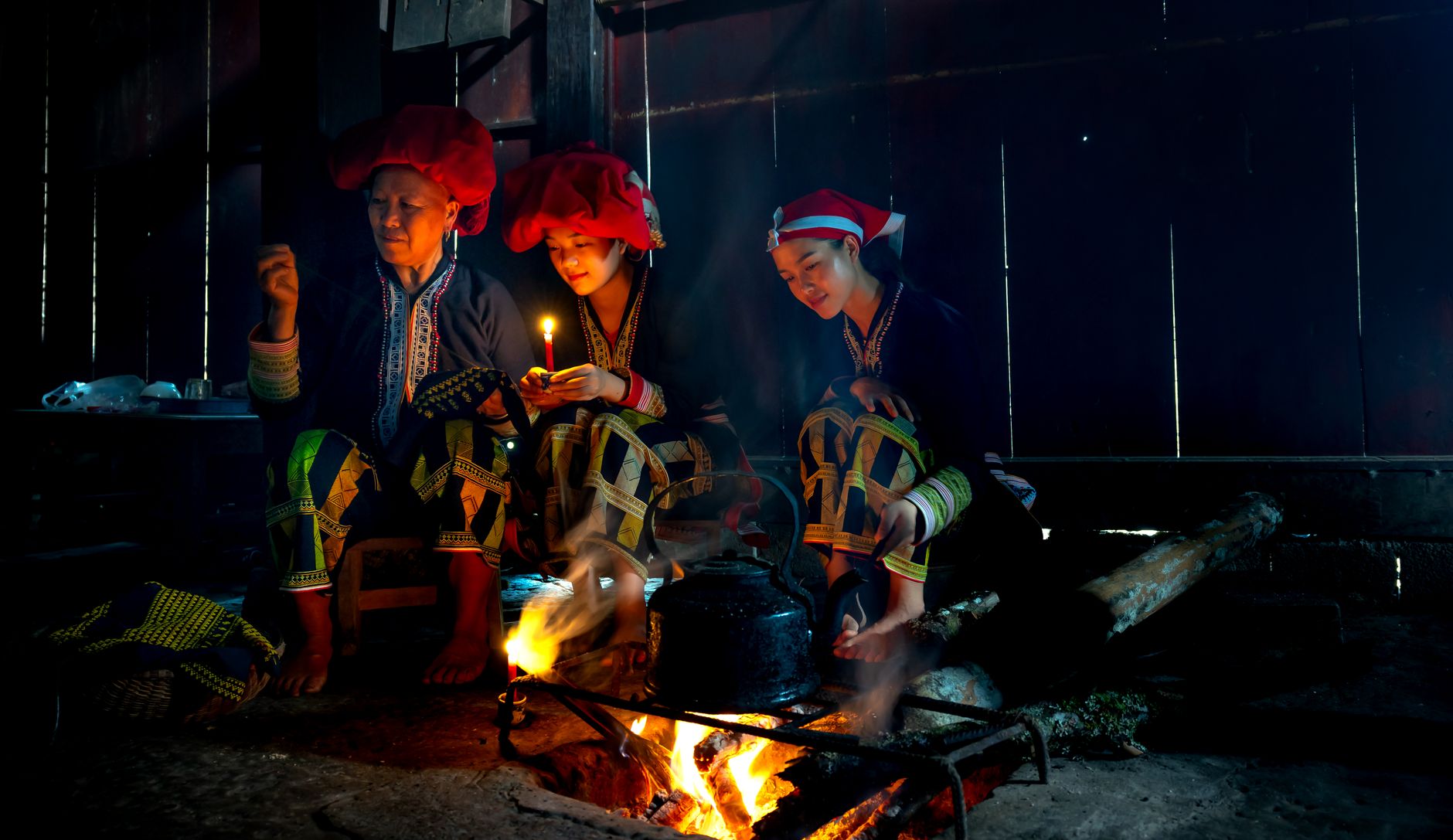 Women in traditional clothing cooking over an open fire indoors, showcasing cultural heritage.