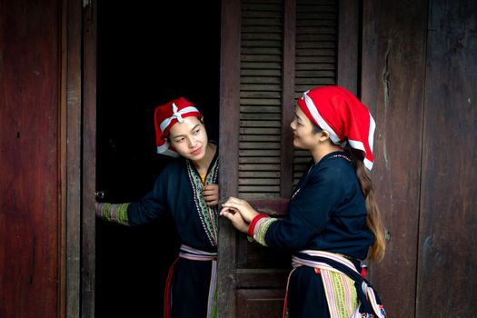 Two women in traditional attire chatting by a wooden doorframe, showcasing cultural fashion.