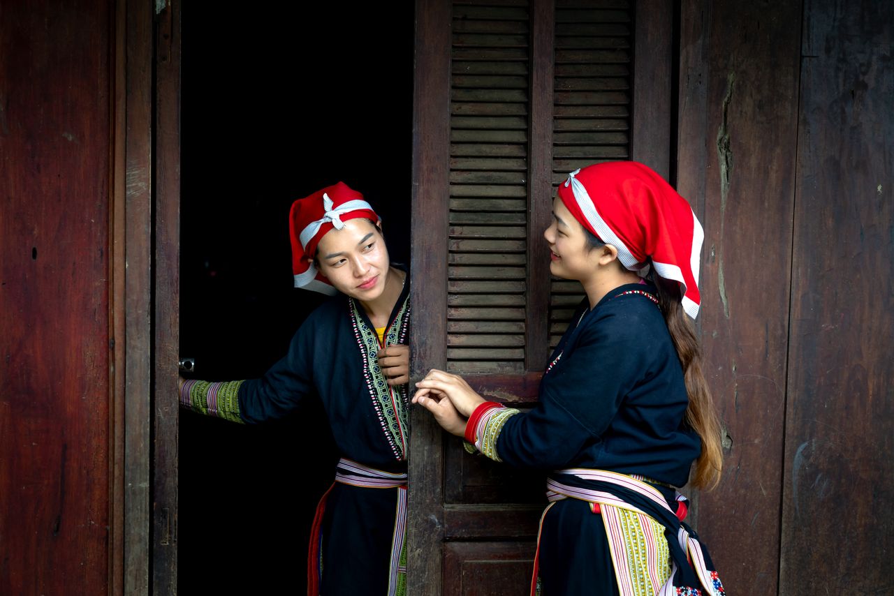 two women in traditional attire chatting by a wooden doorframe showcas