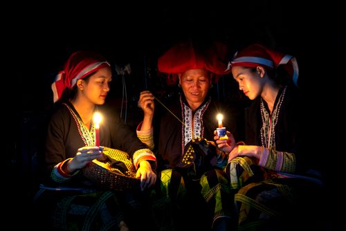 Free Three women sewing traditional patterns by candlelight in a dimly lit setting. Stock Photo