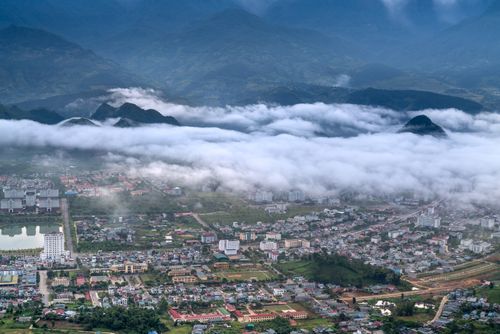 Free Aerial city view with buildings under a blanket of clouds, surrounded by mountains. Stock Photo