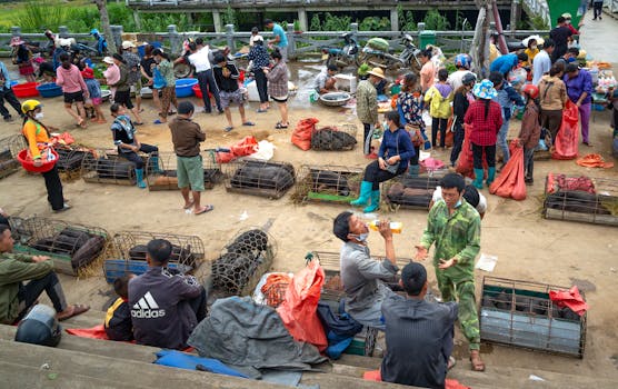 Busy outdoor market scene with merchants selling livestock in cages, attracting diverse people.