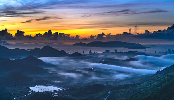 Breathtaking aerial shot of misty mountains and a vibrant sunrise over the ocean horizon.