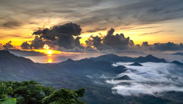 Stunning sunrise view with dramatic clouds and mist over a scenic mountain landscape.