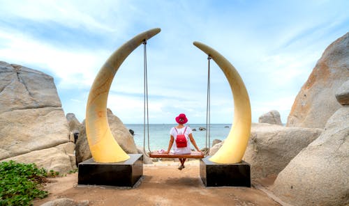 Woman Sitting on a Coastal Swing Hanging Between Two Large Tusks