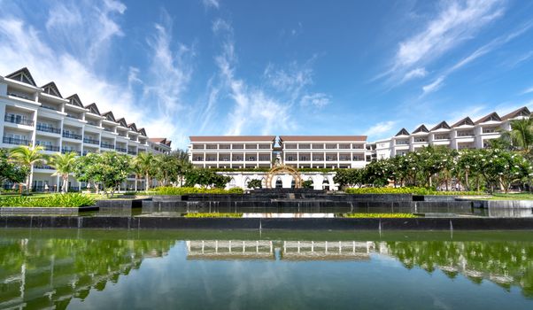 Elegant hotel facade with reflecting pool under a clear blue sky, showcasing architectural beauty.