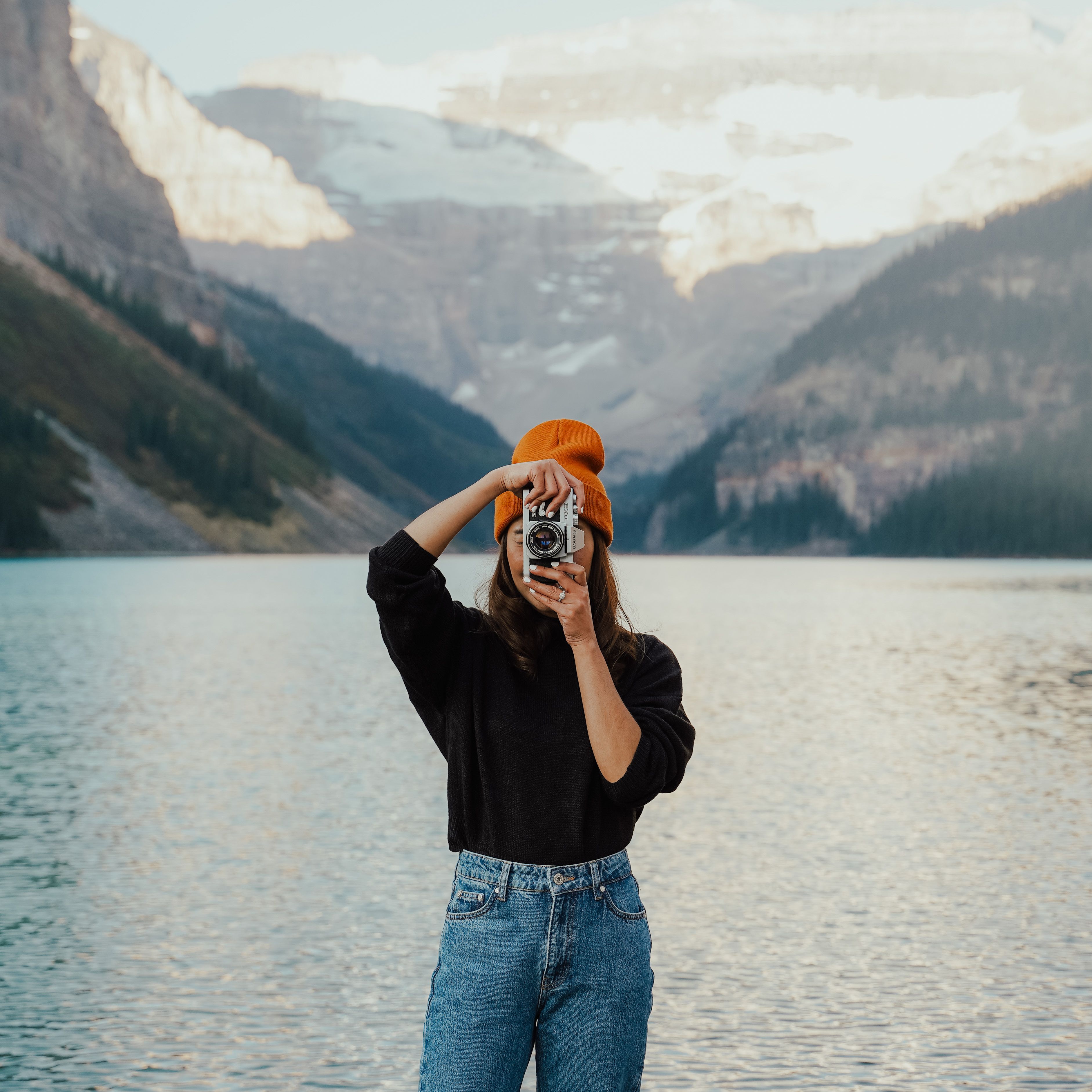 Woman in orange hat photographing a mountain lake with a vintage camera.