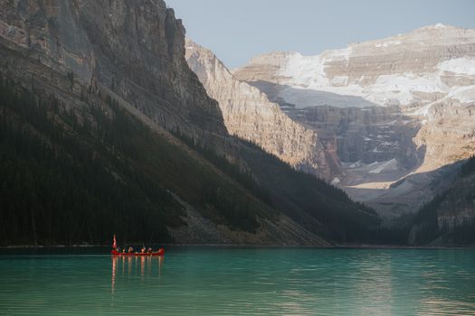 Kayakers paddle on a serene turquoise lake surrounded by towering mountain ranges.