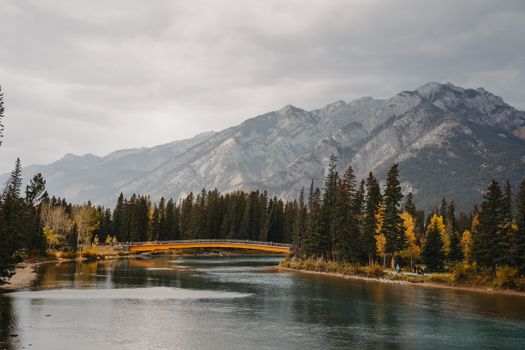 A scenic landscape featuring a river, bridge, and mountain range with cloudy skies.