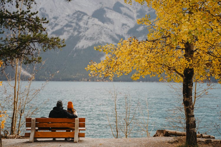 Couple Sitting On A Bench By The Lake In Mountains 