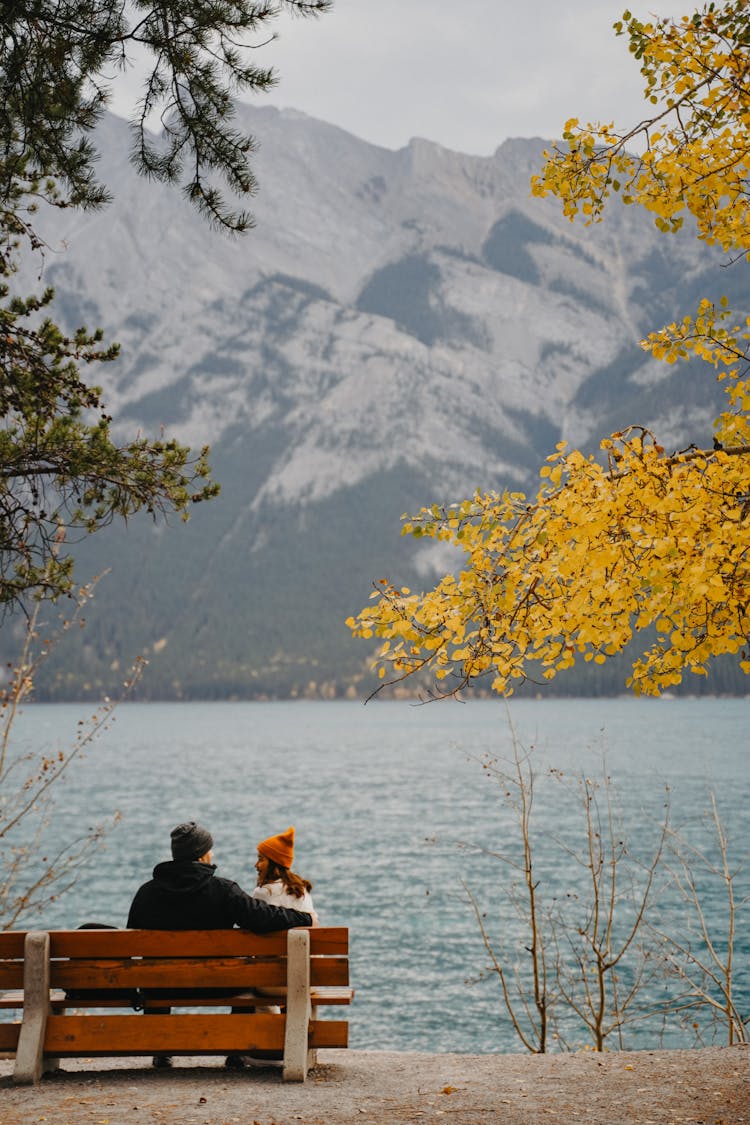 Couple Sitting On A Bench By The Lake In Mountains 