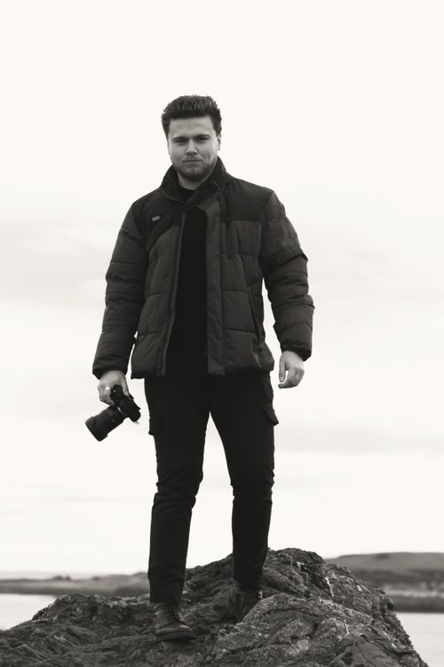 Free A monochrome image showcasing a photographer with a camera standing confidently on a rocky outcrop outdoors. Stock Photo