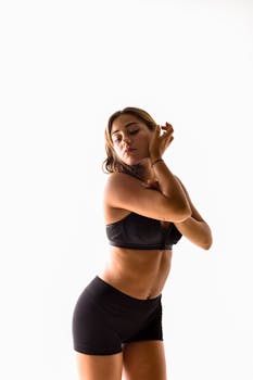 Youthful woman posing gracefully in a studio setting, wearing black lingerie and shorts.
