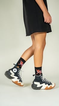Young woman in stylish sneakers and dress showcasing modern fashion on a neutral background.