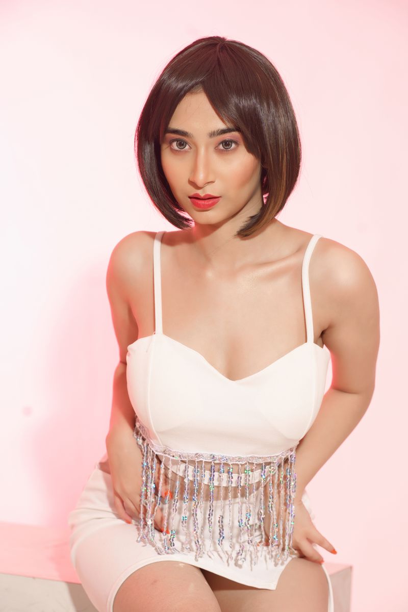 Adult woman with short hair posing elegantly in a white dress with a pink backdrop.