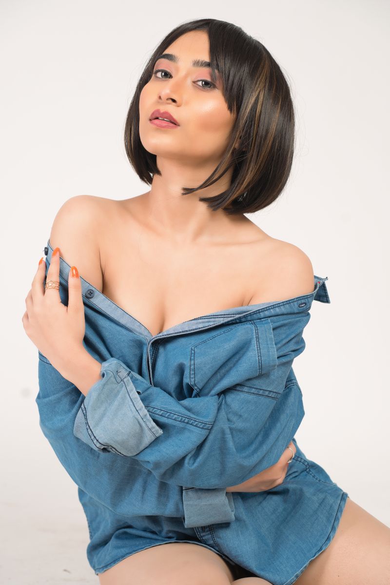 Asian woman with short hair posing in a denim dress in a studio setting.